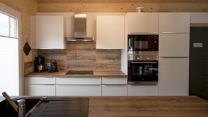 A modern kitchen with white cabinets, a wooden countertop, a built-in oven, and a refrigerator.