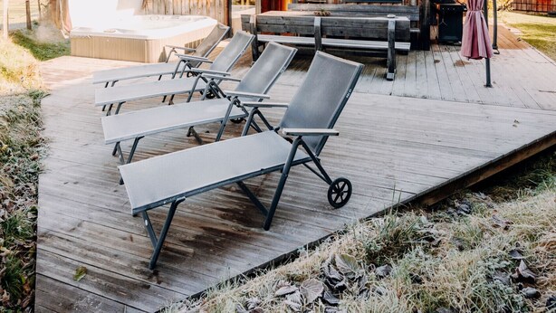 A wooden cabin with a hot tub, lounge chairs, and a deck.