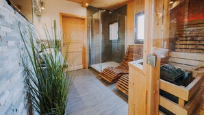 A modern spa room with a glass shower, wooden benches, and a stone wall.