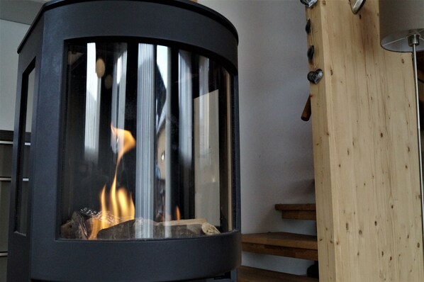 Una chimenea moderna con frente de vidrio, escalones de madera y barandilla de metal.