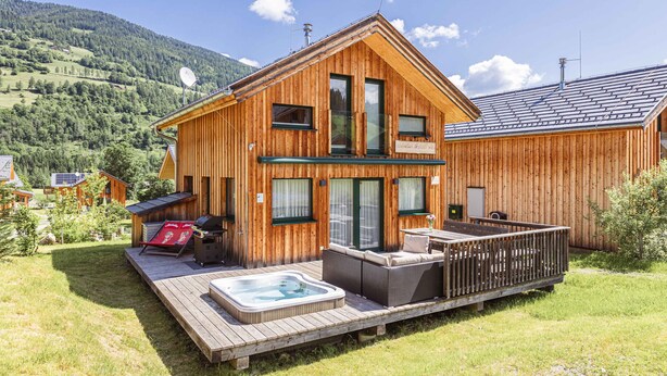 A wooden cabin with a hot tub, outdoor seating, and a deck.