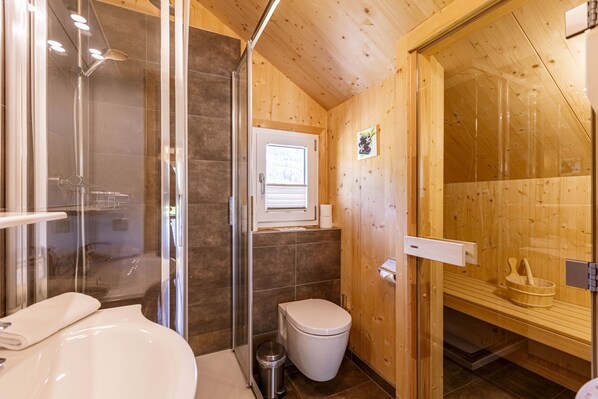 A wooden cabin bathroom with a glass shower enclosure, a white toilet, and a sauna area.