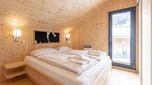 Un dormitorio de cabaña de madera con una cama, dos mesitas de noche, una lámpara de pared y una ventana con vistas al exterior.