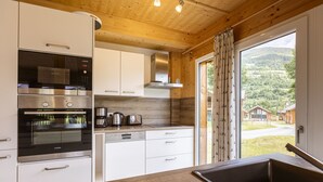 Une cuisine moderne dotée d’appareils électroménagers en acier inoxydable, de meubles blancs et offrant une vue sur un paysage montagneux grâce à une grande fenêtre.