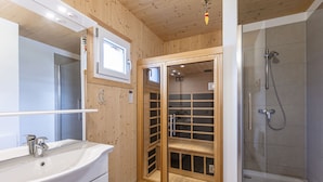 Une salle de bain avec un intérieur en bois, une douche fermée par des parois de verre, un lavabo avec un miroir et une petite fenêtre.