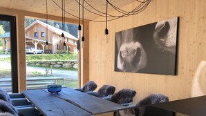 A modern dining area with a wooden table, fur-covered chairs, and a glass bowl. A large painting of a bear's face is on the wall.