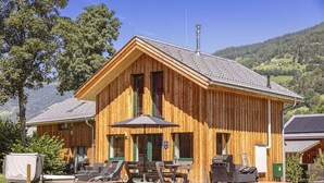A wooden cabin with a deck, outdoor seating, and a grill area.