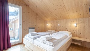 A wooden cabin bedroom with a bed, pillows, and towels neatly arranged.