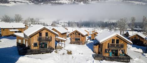 Una hilera de cabañas de madera con balcones, rodeadas de nieve y montañas al fondo.