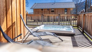 Una terraza de madera con un jacuzzi, sillas de descanso y una cabaña de madera al fondo.