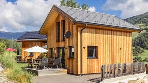 Una cabaña de madera con techo inclinado, paneles solares y un patio con mobiliario exterior.