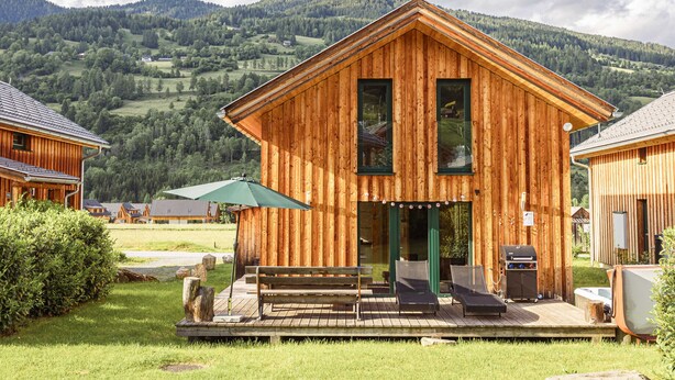 A wooden cabin with a deck, a barbecue, and a view of the surrounding hills. - Chalet # 65a mit 4 Schlafzimmer, IR-Sauna & Whirlpool (St. Georgen am Kreischberg)