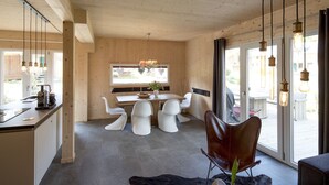 Una cocina moderna con comedor, que cuenta con un ventanal grande, sillas blancas y un sillón de cuero.
