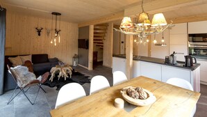 Un interior moderno con una mesa de comedor de madera, sillas blancas, un sofá y una zona de cocina.