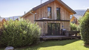 Una cabaña de madera con terraza, barbacoa exterior y antena parabólica.