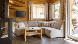 Interior acogedor de una cabaña con techo de madera, un sofá, una mesita, una chimenea y ventanas amplias con cortinas.