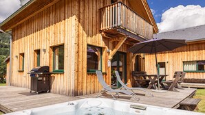 Una cabaña de madera con jacuzzi, sillas de descanso y una parrilla.