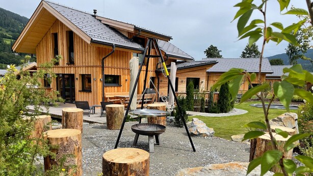 En stuga byggd av trä med en veranda, utomhusmöbler och en eldstad.