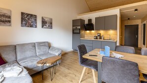 A modern living room with a grey sofa, a wooden coffee table, and a dining area with a wooden table and grey chairs.