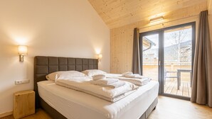 A bedroom with a large bed, wooden walls, and a sliding glass door to an outdoor area.