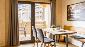 A wooden interior with a table, chairs, a bench, and a view of a building through a glass door.