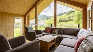A cozy room with a large window, wooden ceiling, and a sofa with cushions.