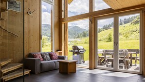 A modern interior with a sofa, wooden table, and a view of a barbecue grill outside.