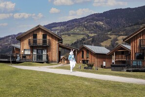Eine Holzhütte mit einem Balkon, eingebettet in eine gebirgige Landschaft unter klarem Himmel.