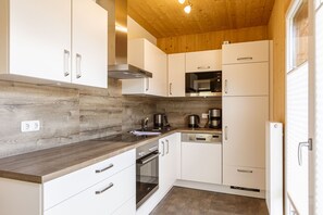 Eine kompakte Küche mit weißen Schränken, einer Holz Arbeitsplatte und einem eingebauten Backofen.