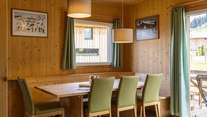 Un intérieur en bois avec une table et des chaises, des tableaux encadrés aux murs et une fenêtre avec des rideaux.