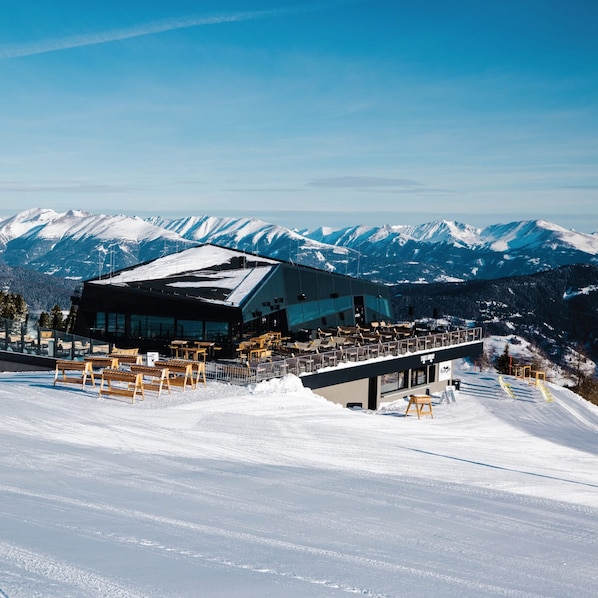 A modern ski resort building with a glass facade, surrounded by snow-covered mountains.