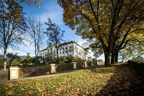 Ein großes Gebäude mit einer symmetrischen Fassade, umgeben von einem Holzzaun und Bäumen mit Herbstlaub.