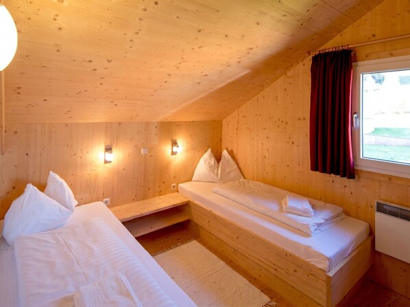 Una habitación tipo cabaña de madera con dos camas, una ventana con cortinas y luces fijadas a la pared.
