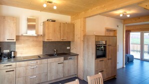 A modern kitchen with wooden cabinets, a stainless steel sink, and a built-in oven. There is a dining area with a wooden table and chairs.