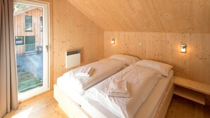 A wooden cabin bedroom with a bed, a window, and a wall-mounted light fixture.