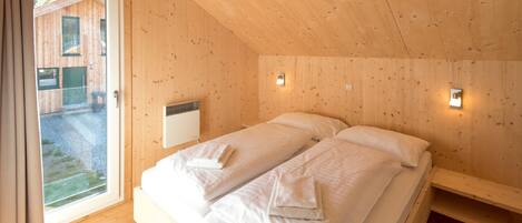 Un dormitorio de cabaña de madera con una cama, un ventanal y una lámpara fijada a la pared.