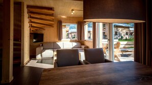 A wooden interior with a dining area, sofa, and large window.