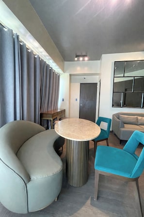 A modern living room with a round table, teal chairs, a gray sofa, and a large mirror on the wall. - One Madison Towers (Iloilo)