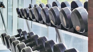 A gym with a rack of dumbbells and a view of a cityscape through large windows. - One Madison Towers (Iloilo)