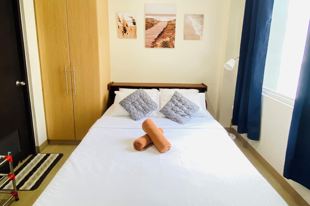 A neatly made bed with two pillows, a wooden wardrobe, and three wall art pieces.