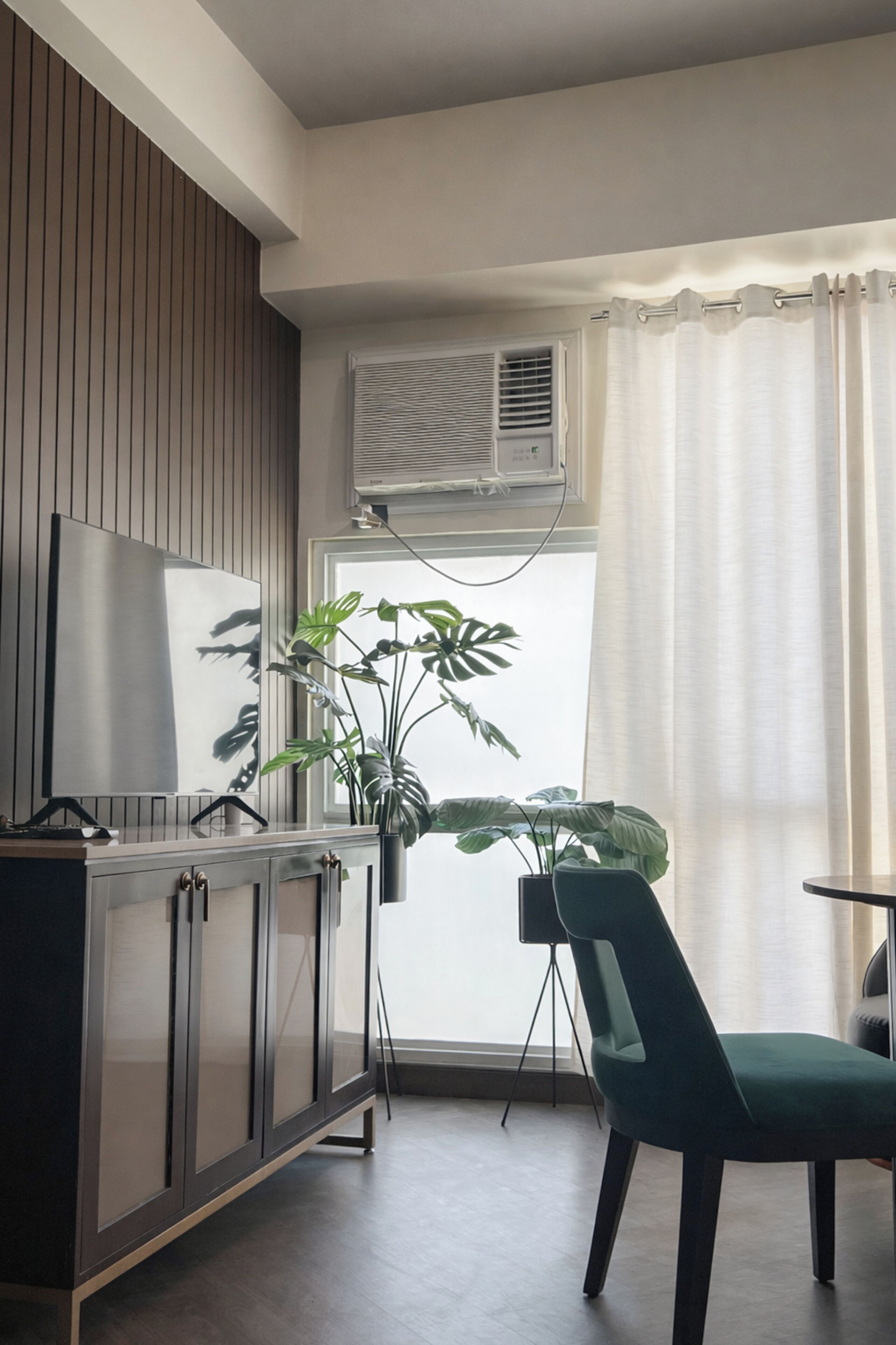 A modern room with a wooden panel wall, a flat-screen TV, a potted plant, a green chair, and an air conditioning unit.