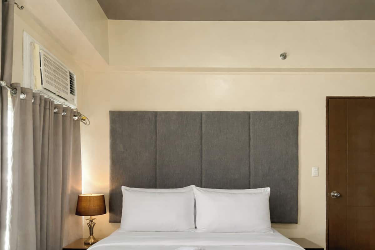A hotel room with a large bed, a headboard, a nightstand with a lamp, and a door.
