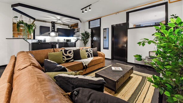 A modern living room with a brown leather sofa, a coffee table, and a kitchen in the background. - Trendy, Arty, 3BR in Heart of Hipster Hackney! (London)