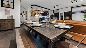 A modern dining area with a wooden table set for four, a brown leather couch, and a kitchen in the background. - Trendy, Arty, 3BR in Heart of Hipster Hackney! (London)