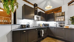 A modern kitchen with dark cabinets, a stainless steel range hood, and a variety of appliances including a microwave and toaster. - Trendy, Arty, 3BR in Heart of Hipster Hackney! (London)