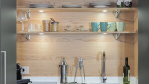 A kitchen with wooden shelves, black pots, clear glassware, and a coffee maker.