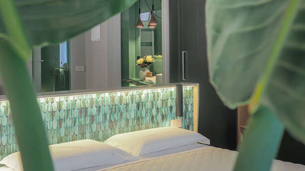 A bedroom with a bed, a mirror, and a green plant in the foreground.