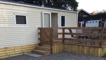 Una casa móvil con una terraza de madera, un pequeño espacio de estar al aire libre y un camino de entrada de grava.
