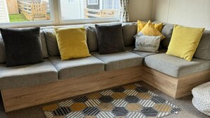 A sectional sofa with multiple cushions, a patterned rug, and a window with a view of a backyard. - Highland Chalet Retreat in Boat of Garten (Boat of Garten)