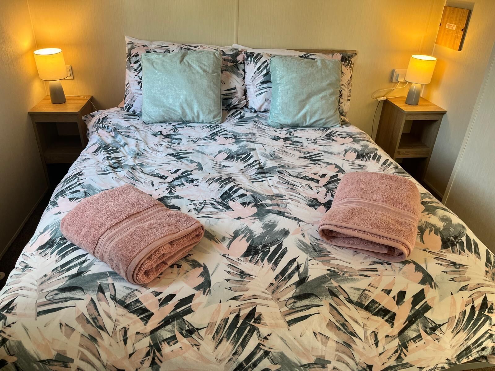 Una cama con colcha estampada, dos almohadas y dos lámparas de noche.